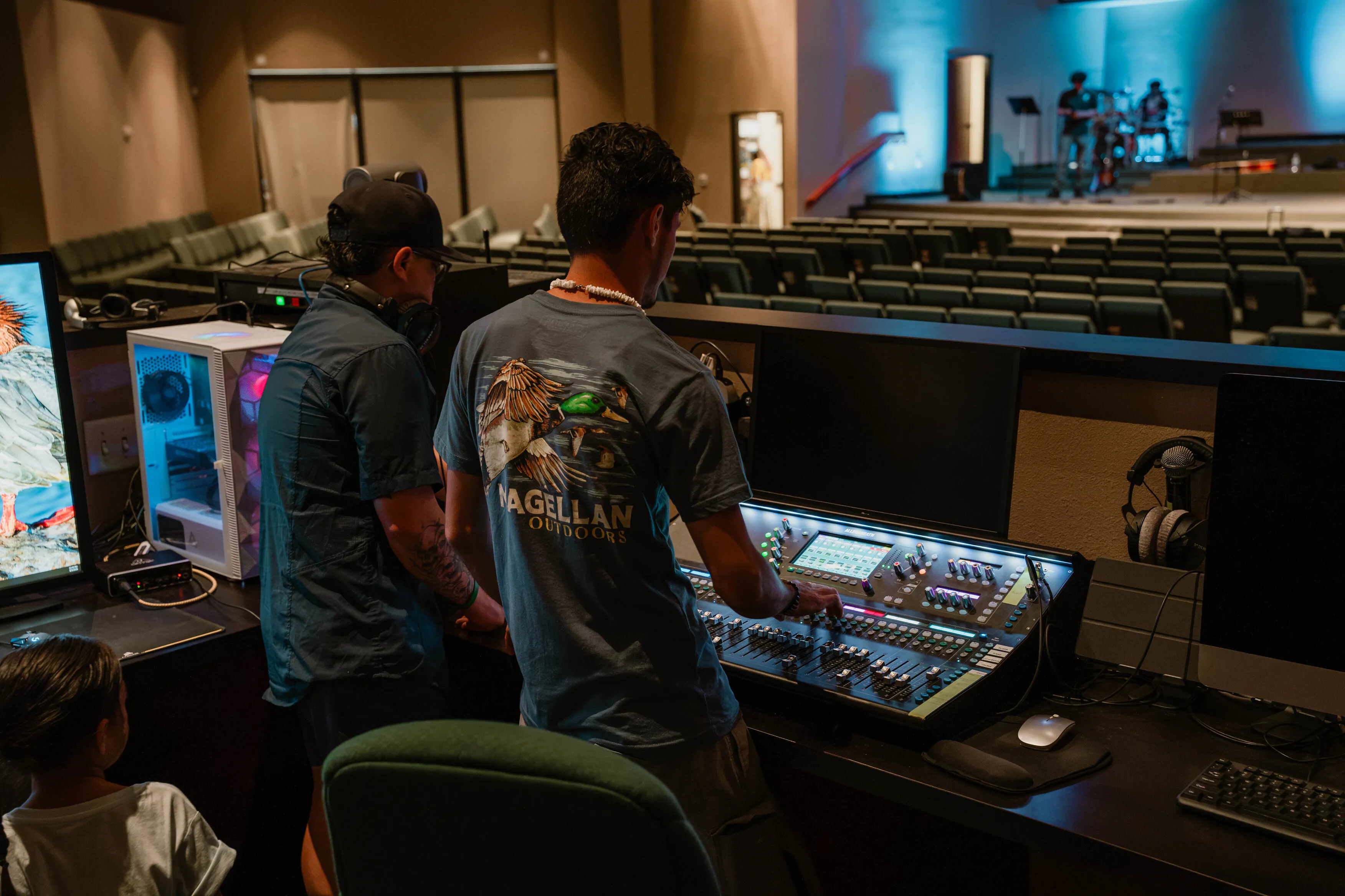 Dos personas del equipo de producción operan la consola de sonido al fondo del auditorio