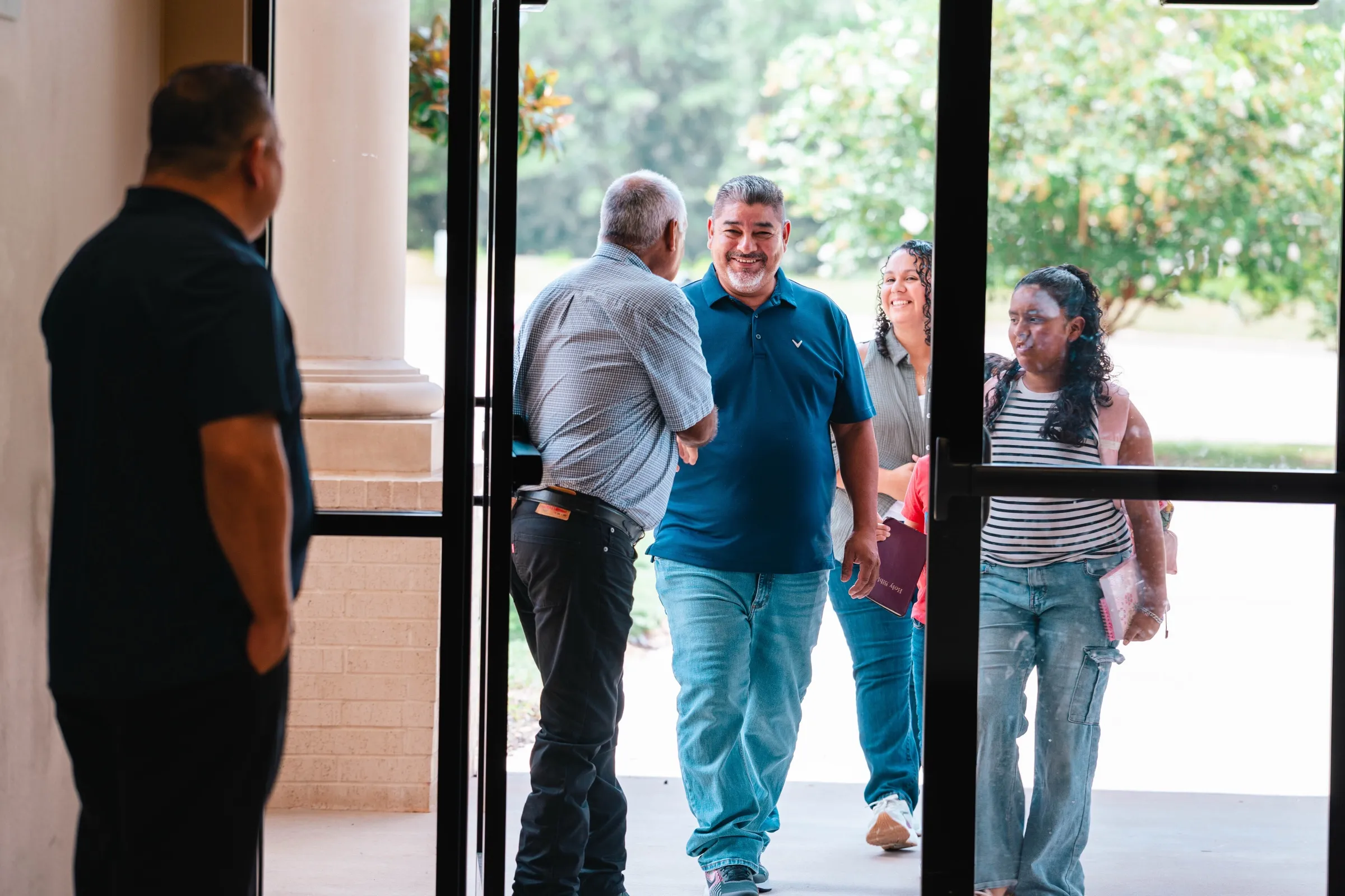 Varias personas entran caminando por la puerta principal del templo y se saludan