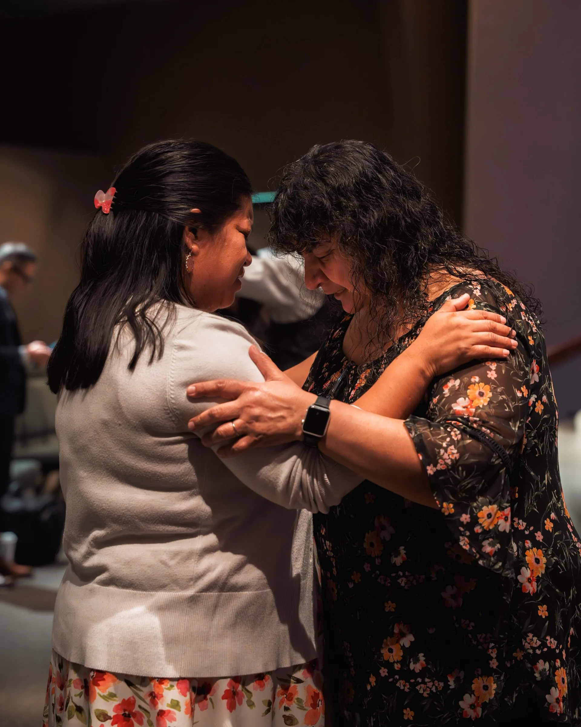 Dos mujeres oran juntas de pie, una con las manos sobre los hombros de la otra