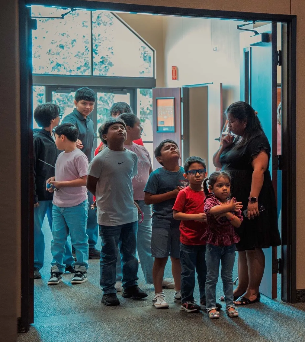 Una fila de niños entra al salón acompañada por una voluntaria
