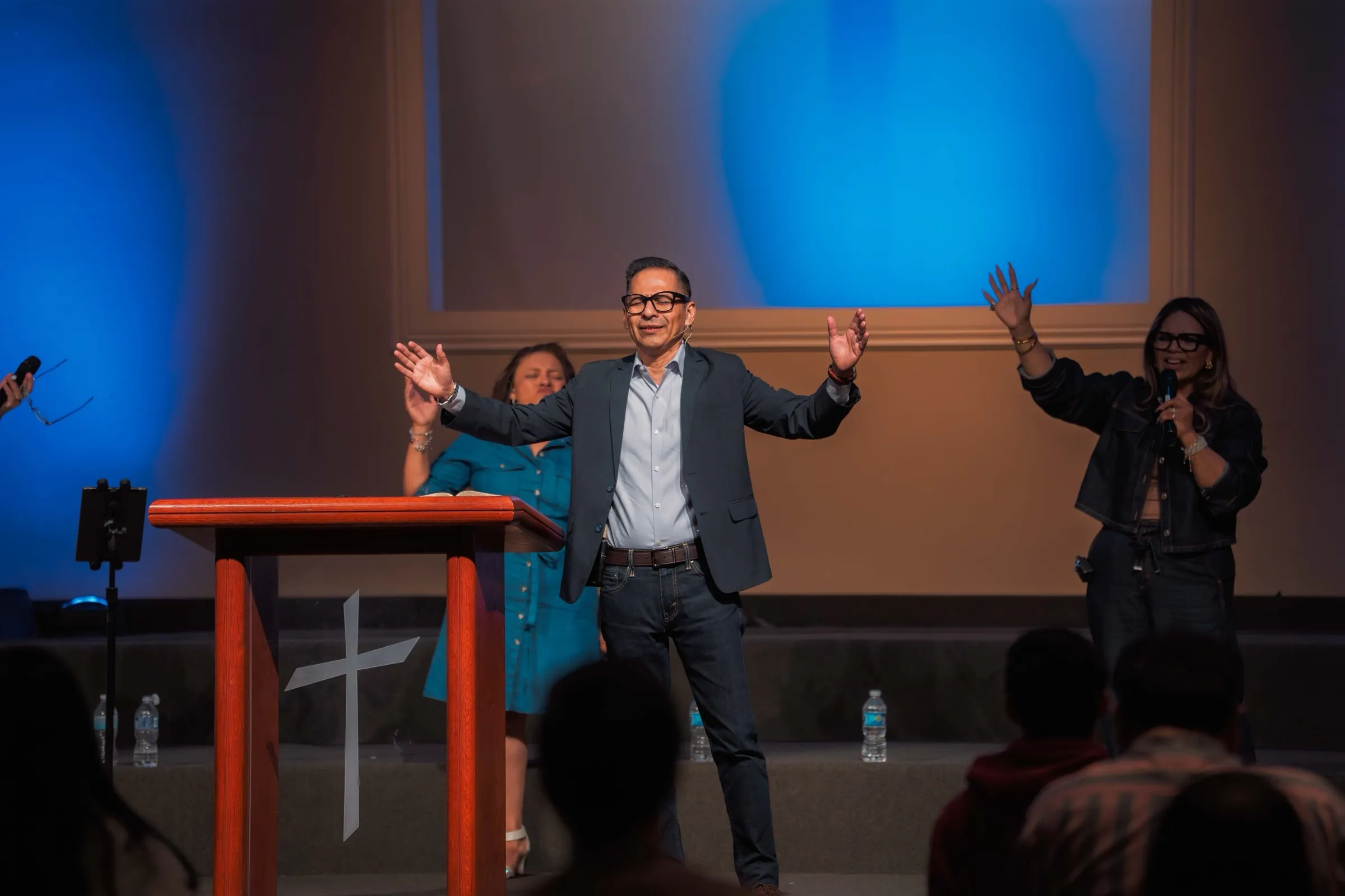 El pastor abre los brazos desde la plataforma durante el servicio