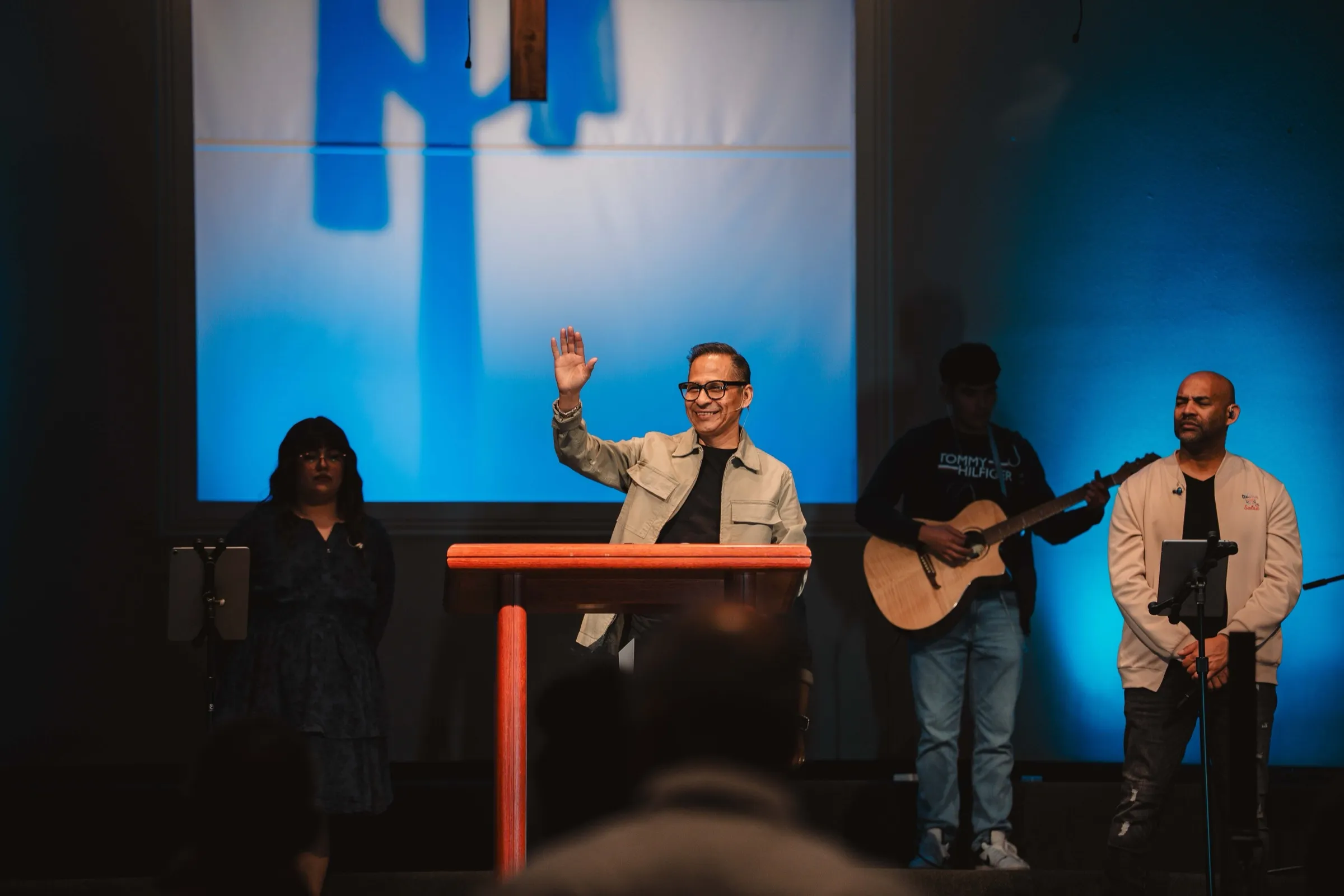 El pastor saluda con la mano desde el púlpito al comenzar el servicio