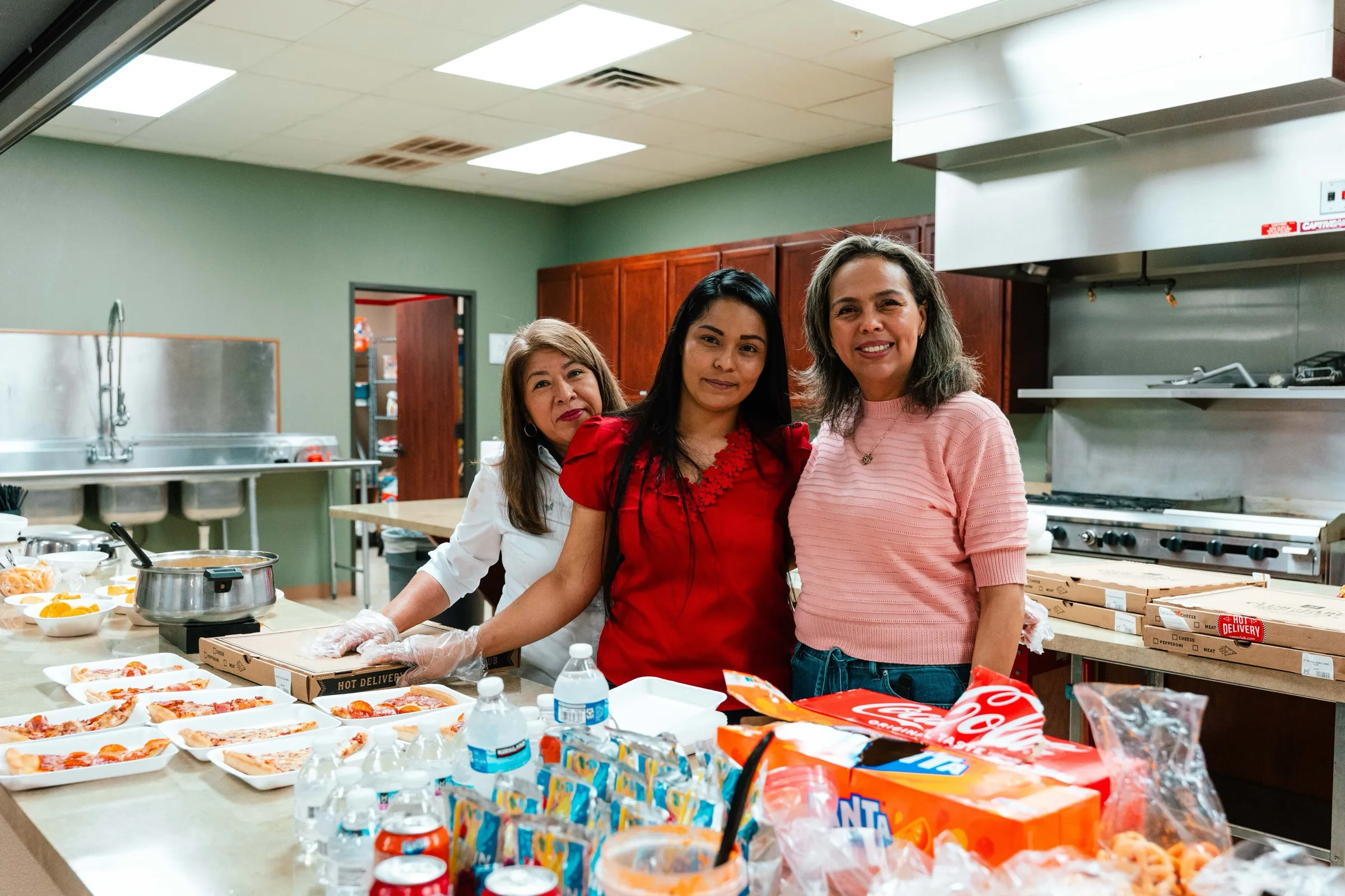 Tres mujeres sonríen mientras preparan la comida en la cocina de la iglesia